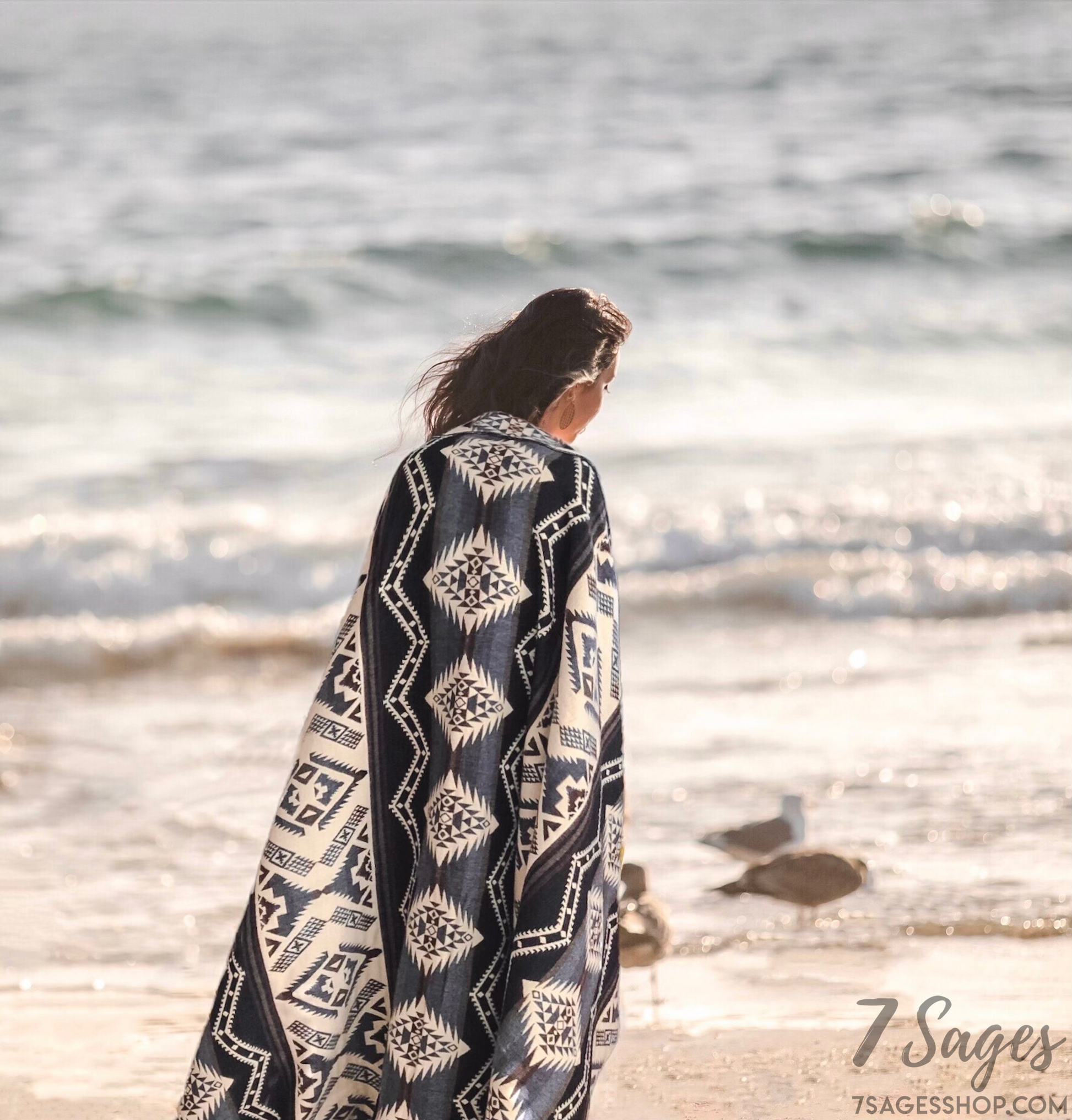 Alpaca wool blanket draped over shoulders of woman with brown hair walking at the beach during sunset