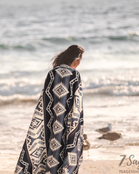 Alpaca wool blanket draped over shoulders of woman with brown hair walking at the beach during sunset