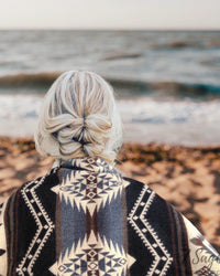 Luxury Alpaca Wool Blanket draped over shoulders of woman at beach with blonde hair during sunset